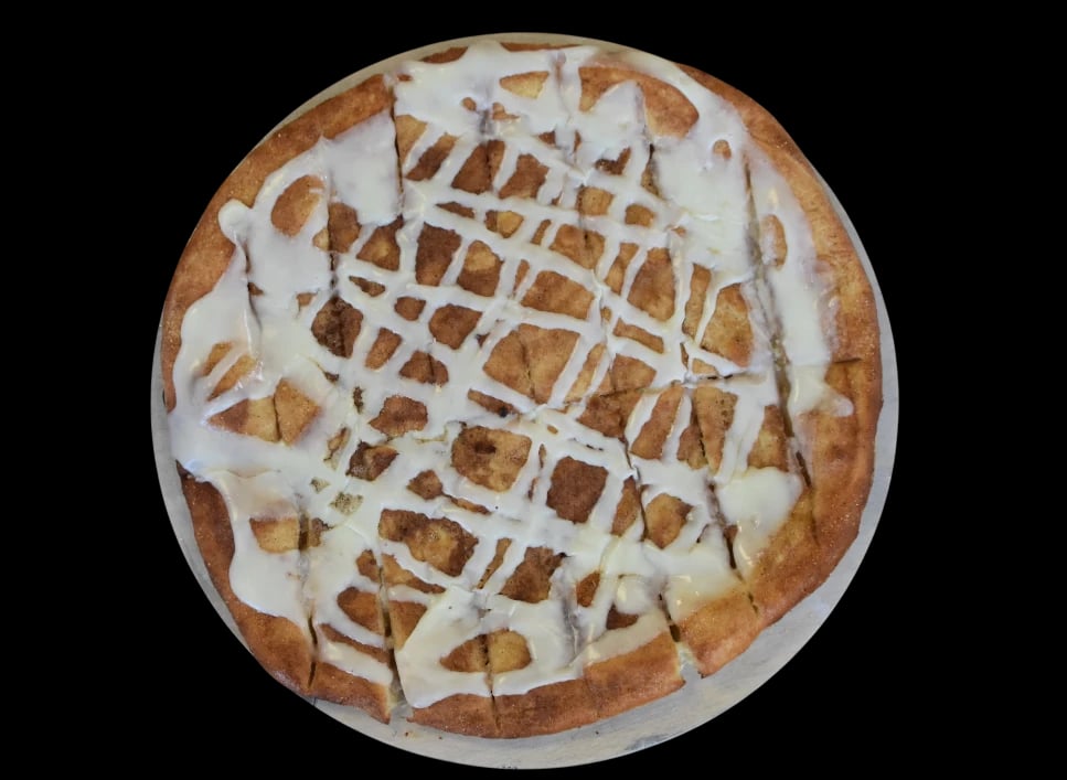 Cinnamon roll pizza topped with icing, cut into slices.